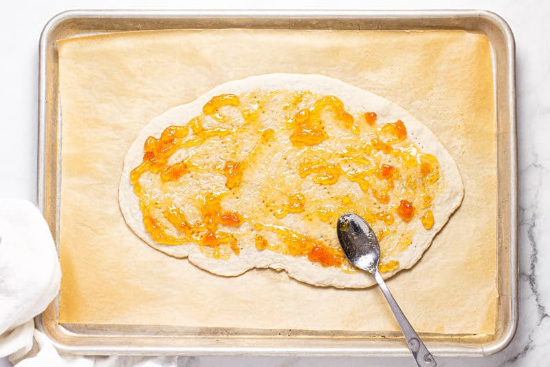 Overhead shot of a baking sheet with flatbread dough spread with apricot jam 