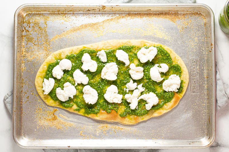 A flatbread crust with fresh spinach pesto and fresh mozzarella on it 
