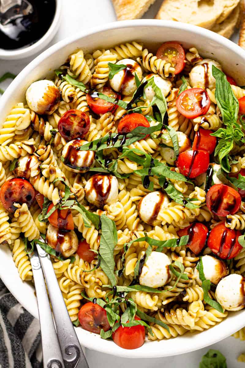 Overhead shot of a Caprese pasta salad in a white serving bowl drizzled with balsamic glaze
