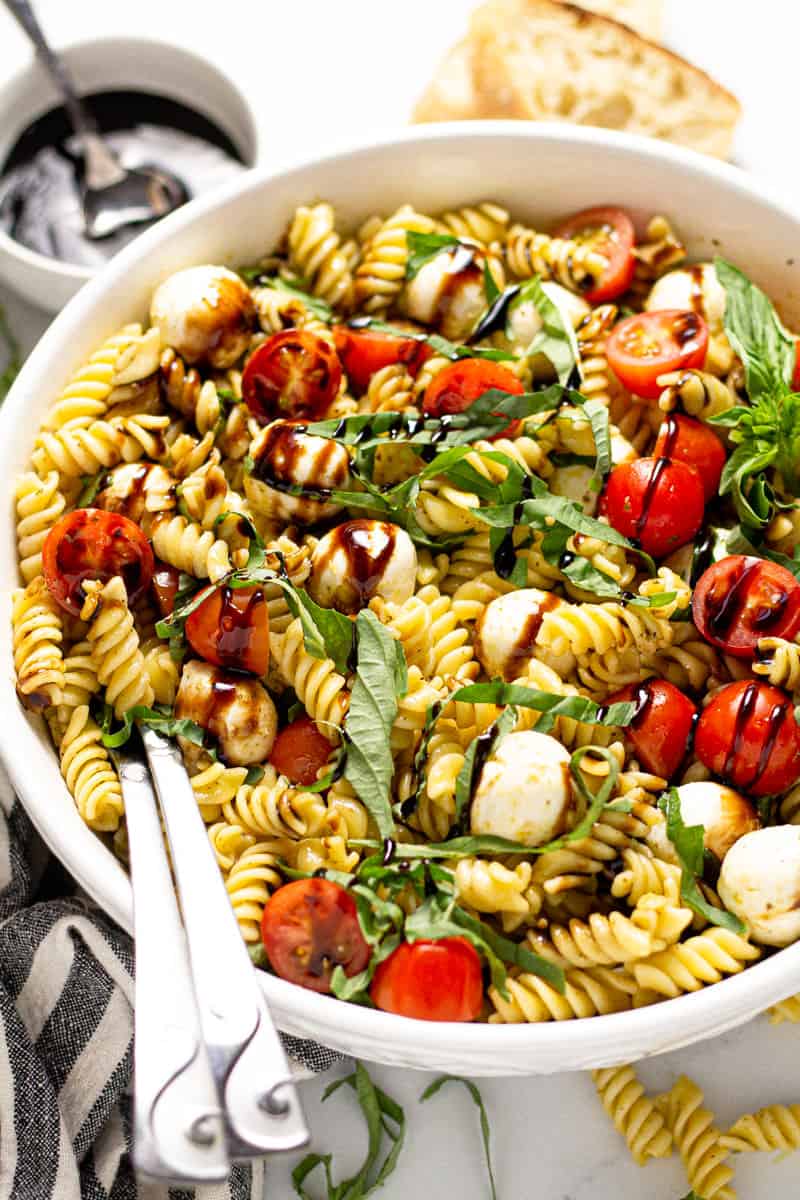 Close up shot of a Caprese pasta salad in a white serving bowl drizzled with balsamic glaze