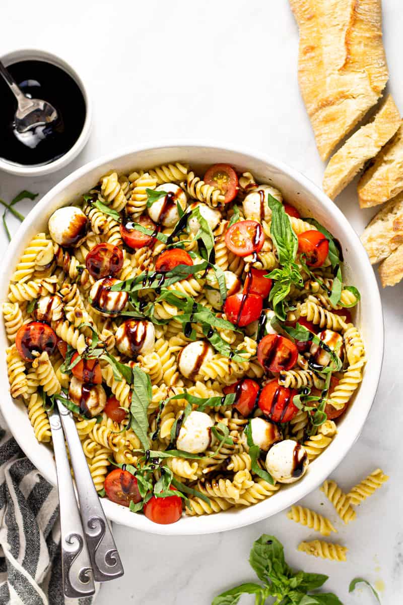 Overhead shot of a Caprese pasta salad in a white serving bowl drizzled with balsamic glaze