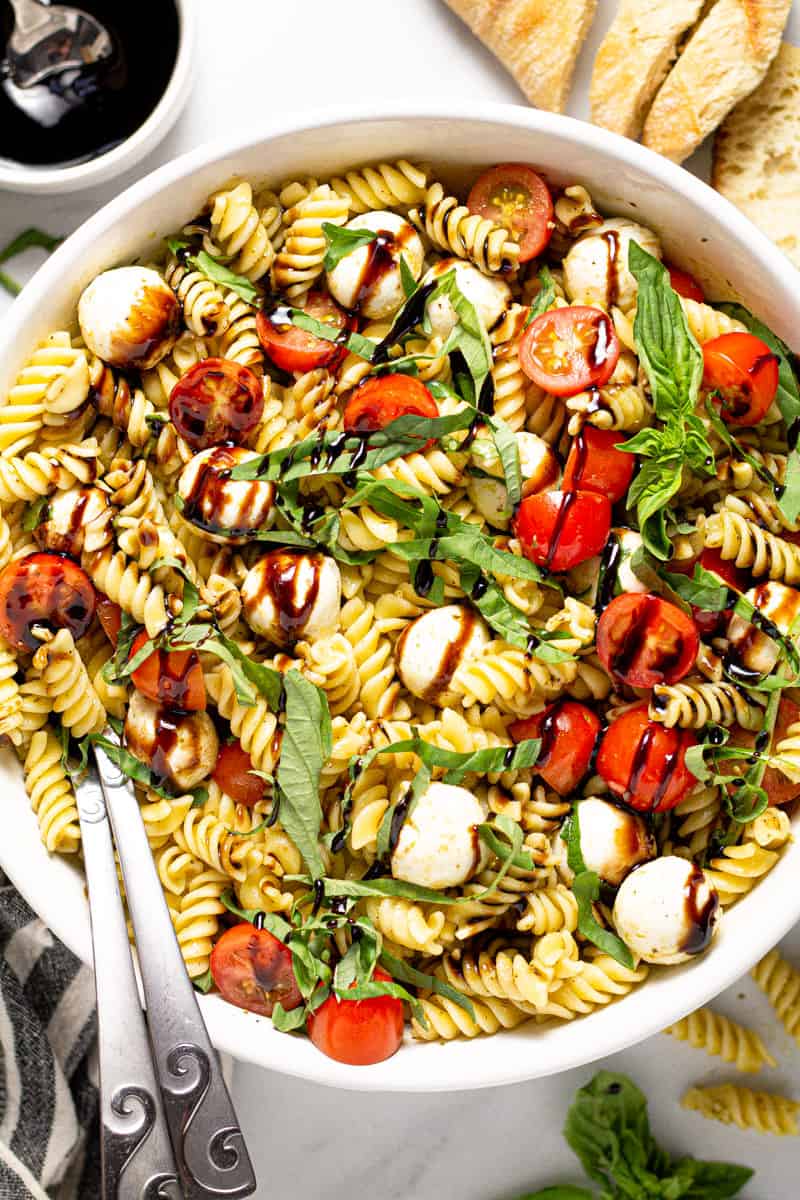 Overhead shot of a Caprese pasta salad in a white serving bowl drizzled with balsamic glaze