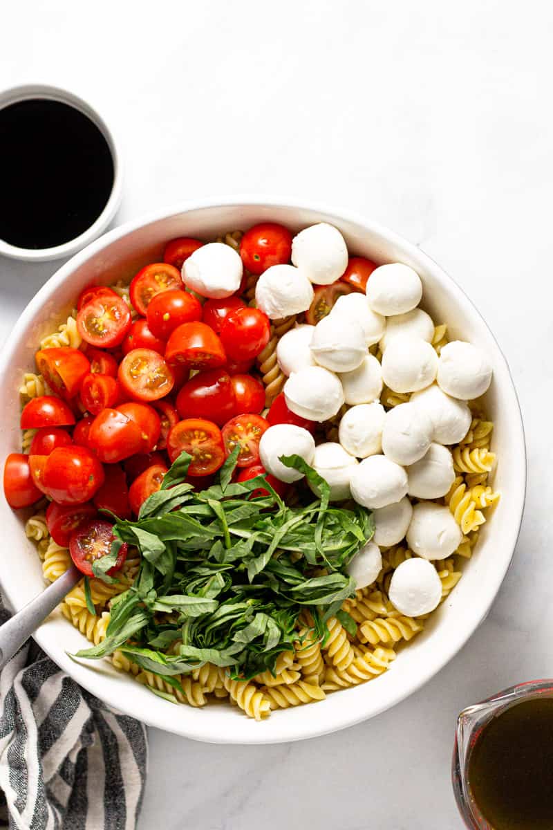 Large white bowl filled with ingredients to make a Caprese pasta salad