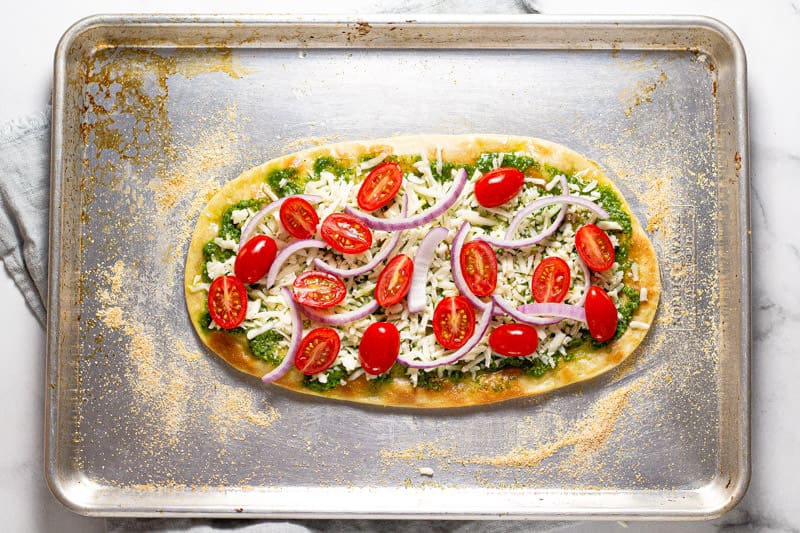 Greek flatbread pizza on a baking sheet with onions and tomatoes