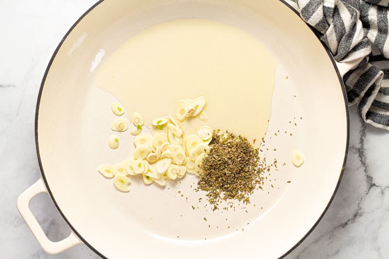 Large white pan with fresh sliced garlic olive oil and dried oregano