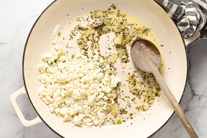 Large white pan filled with sauteed garlic dried oregano and crumbled feta cheese