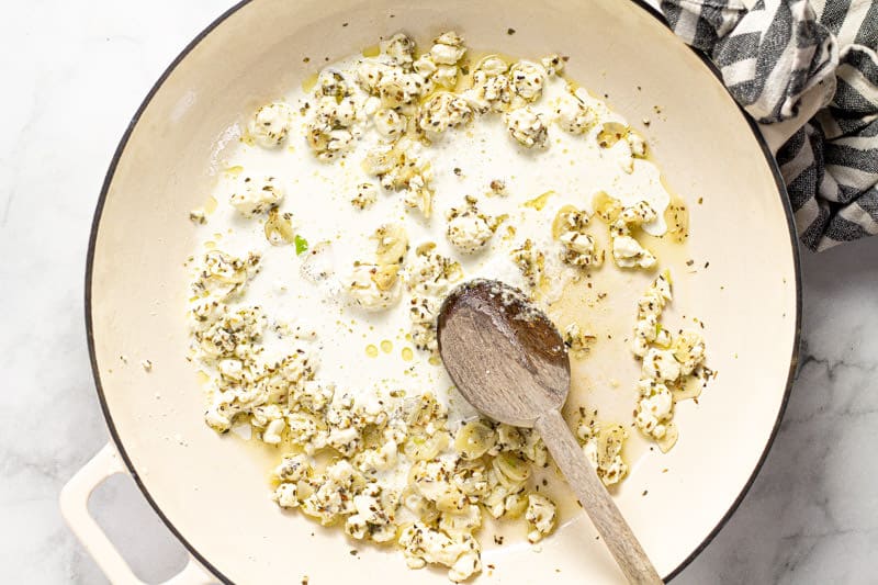 Large white pan filled with sauteed garlic dried oregano and feta sauce