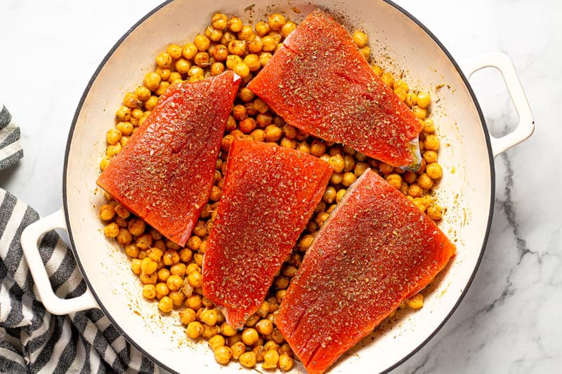 Large white pan filled with seasoned garbanzo beans and 4 salmon fillets