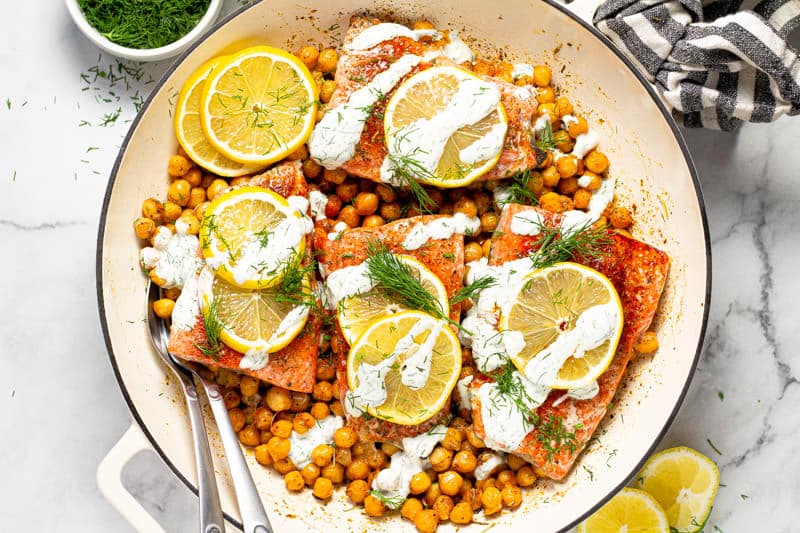 Overhead shot of a white pan filled with Mediterranean baked salmon and roasted chickpeas drizzled with yogurt sauce
