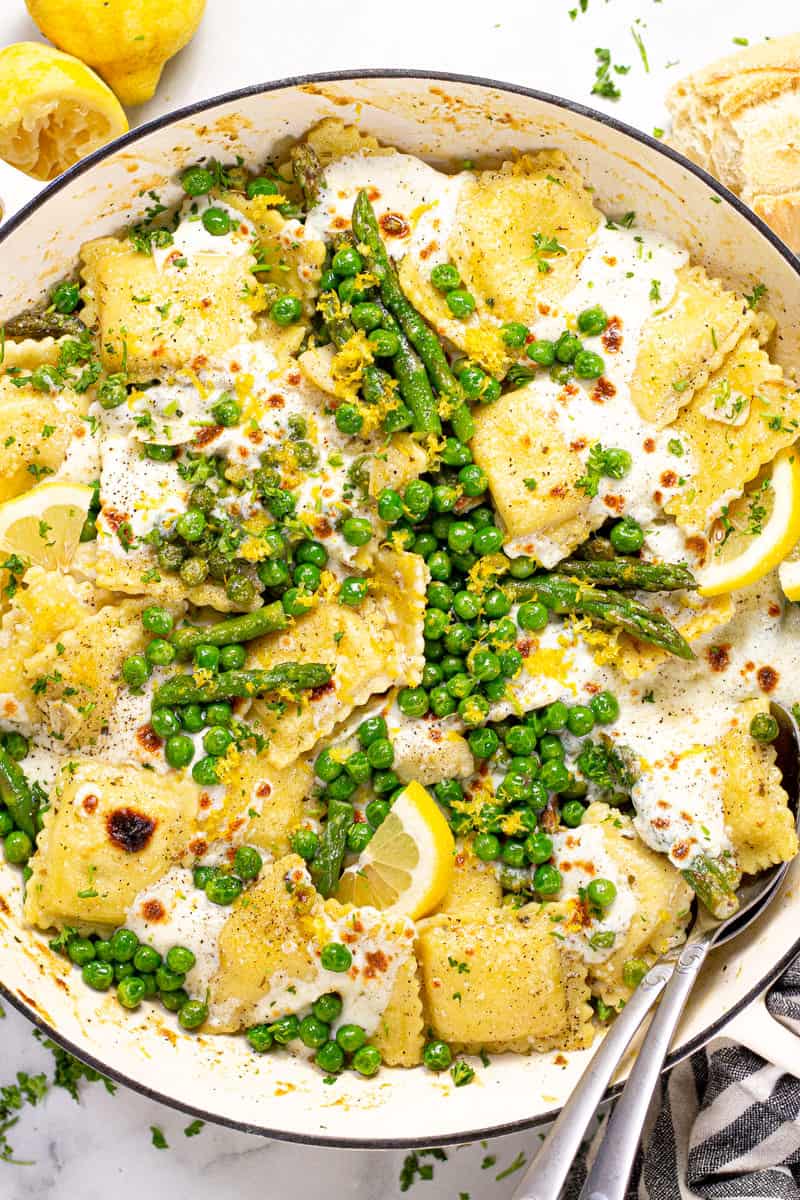 Overhead shot of a large white pan filled with spring ravioli with asparagus peas and cheese