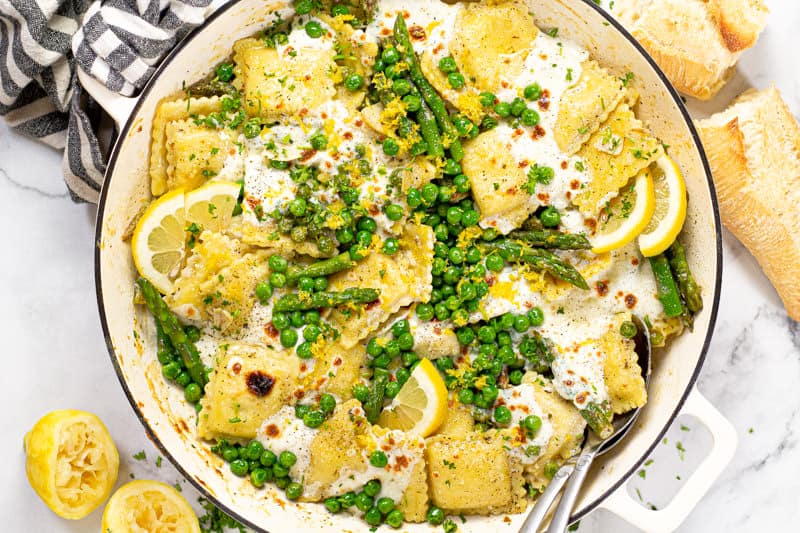 Overhead shot of a large white pan filled with spring ravioli with asparagus peas and cheese