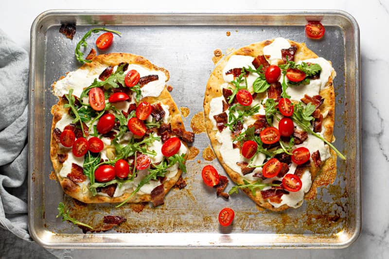 Overhead shot of a baking sheet with two California BLT flatbreads garnished with arugula 