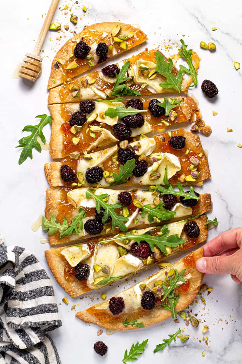 Brie and blackberry flatbread garnished with arugula on a white marble counter top