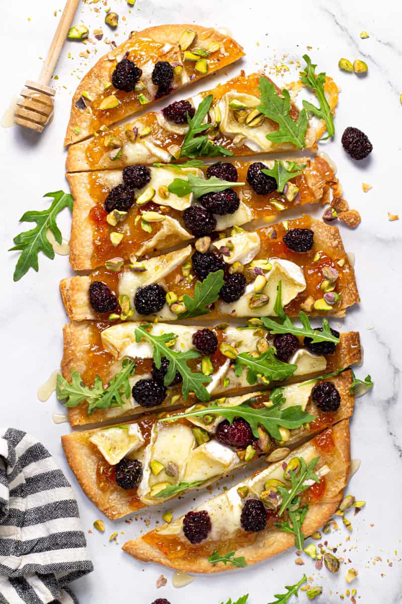 Brie and blackberry flatbread garnished with arugula on a white marble counter top
