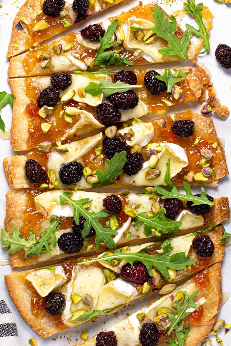 Brie and blackberry flatbread garnished with arugula on a white marble counter top