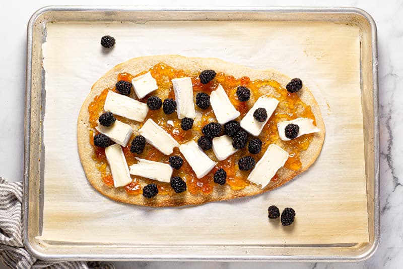 Baking sheet with a flatbread crust spread with apricot preserves brie and blackberry