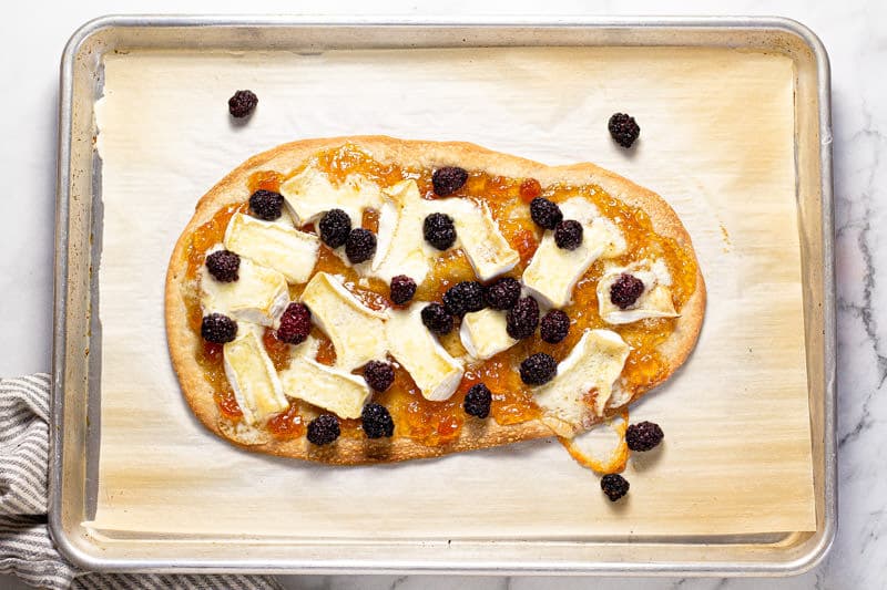 Baking sheet with a flatbread crust spread with apricot preserves brie and blackberry