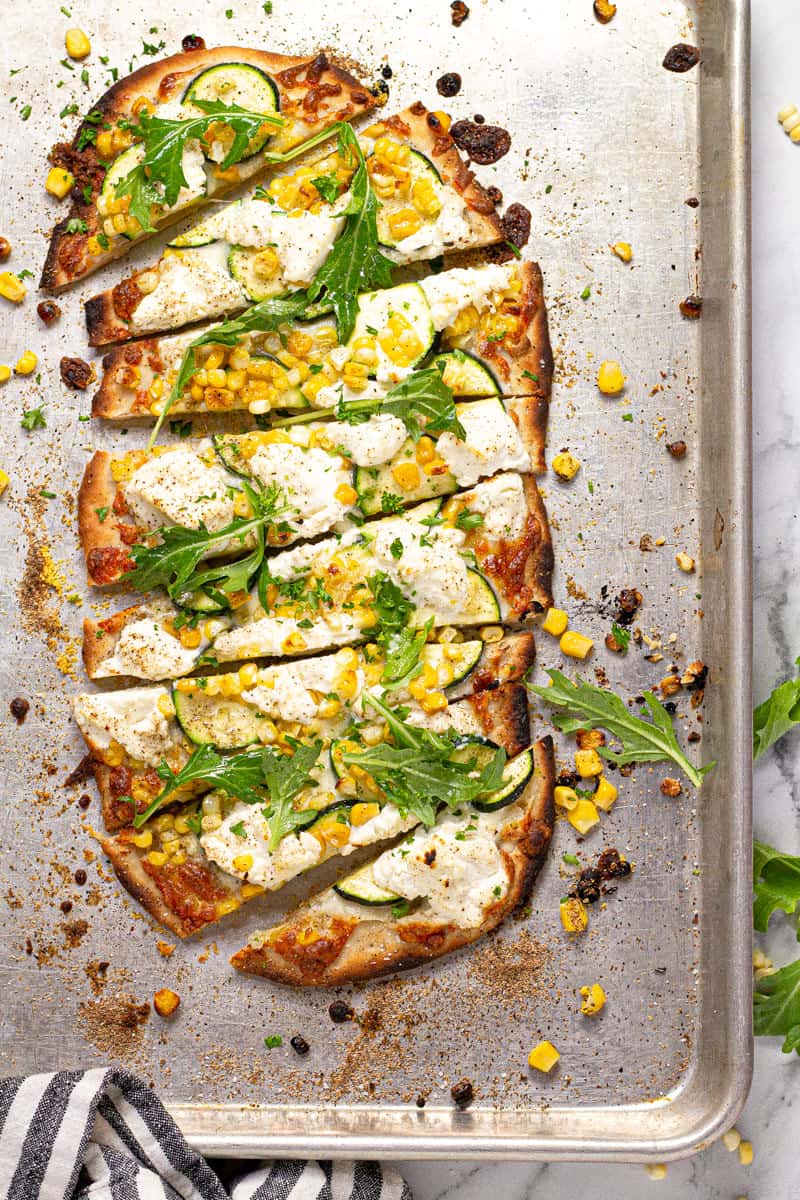 Overhead shot of a vegetable flatbread on a baking sheet sliced and ready to eat