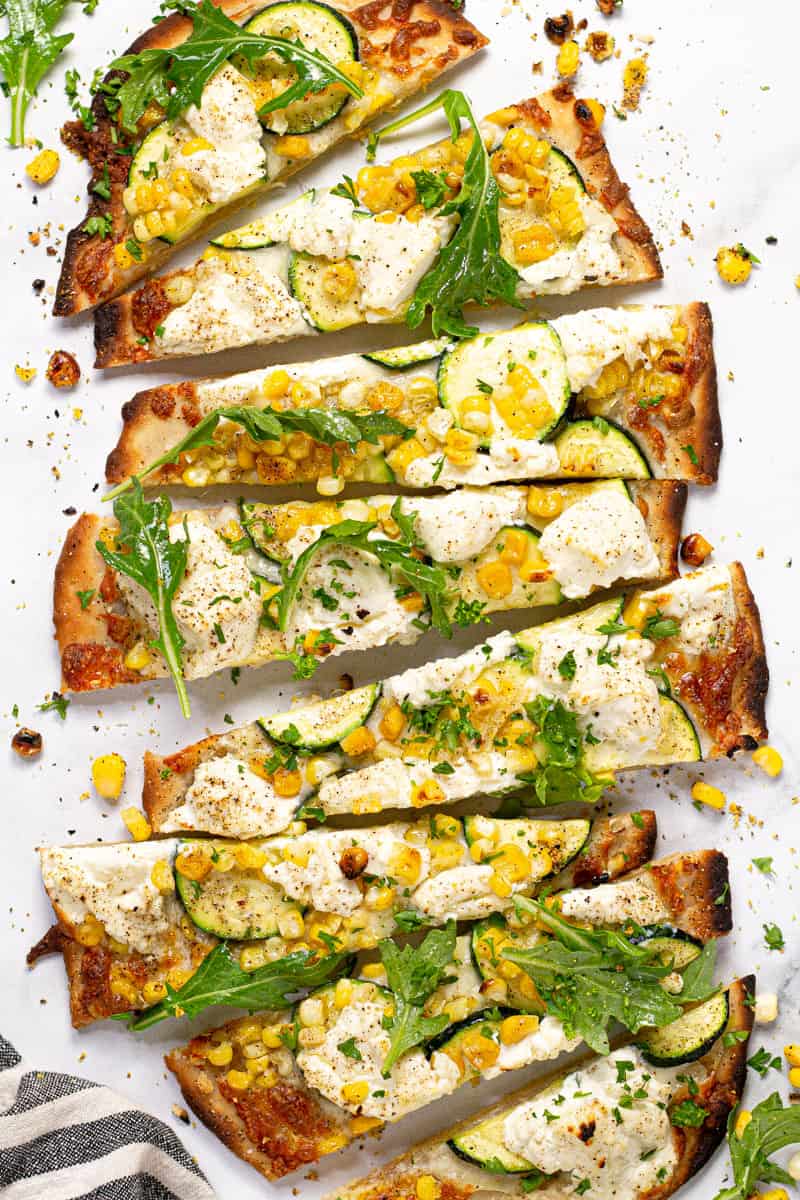 Overhead shot of a vegetable flatbread on a white marble counter top sliced and ready to eat