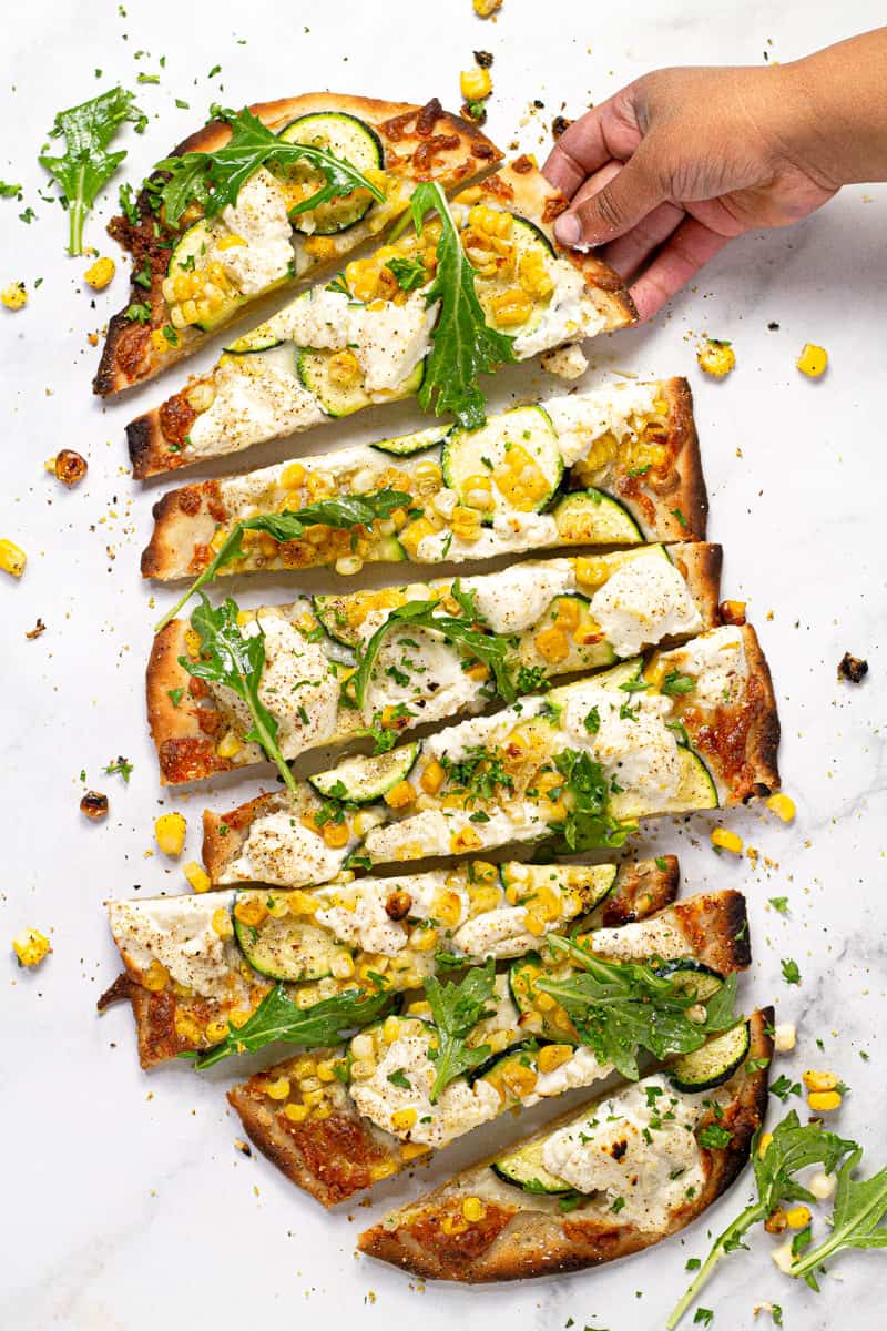 Overhead shot of a vegetable flatbread on a white marble counter top sliced and ready to eat