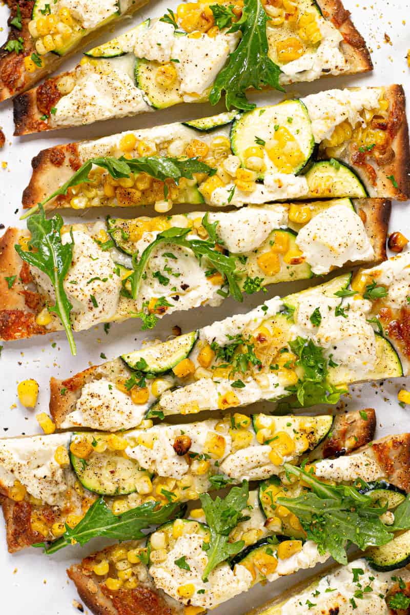 Close up of a vegetable flatbread on a white marble counter top sliced and ready to eat