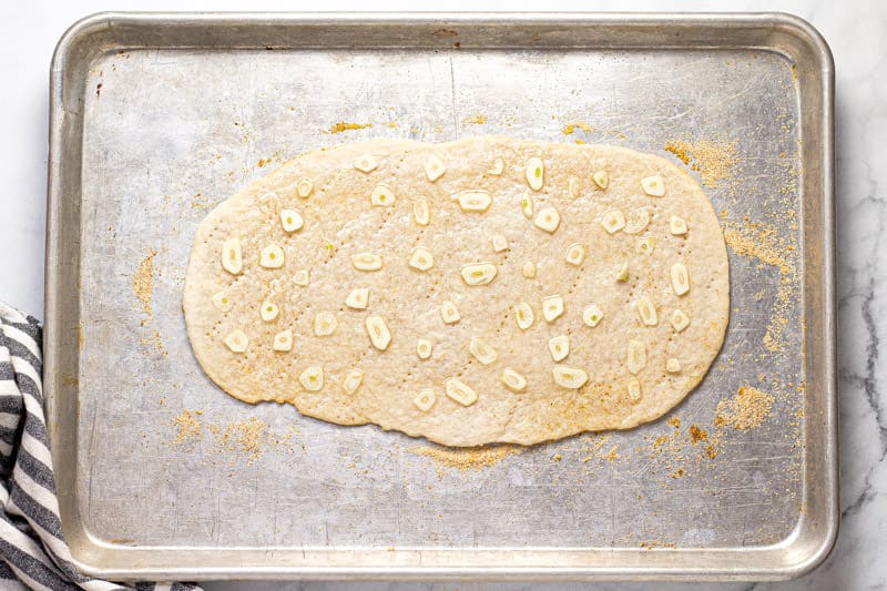 Baking sheet with a flatbread crust with sliced garlic and olive oil on it