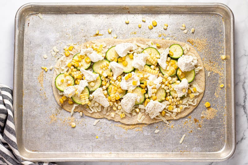 Baking sheet with a corn zucchini and ricotta flatbread on it