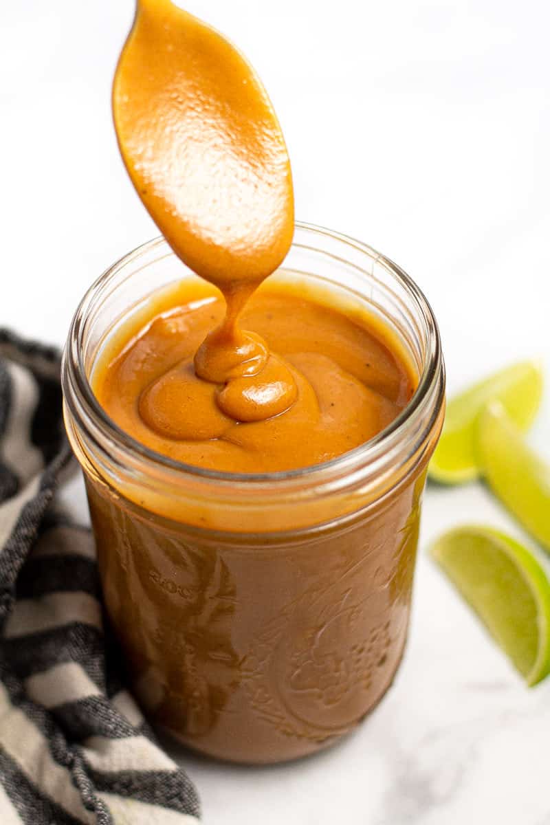 Close up shot of a peanut sauce being drizzle into a mason jar with a spoon 