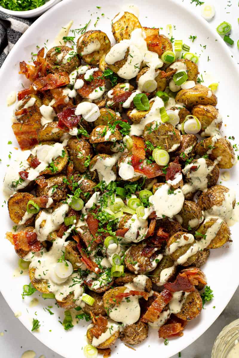 Overhead shot of a large serving platter with roasted potato salad garnished with bacon and parsley