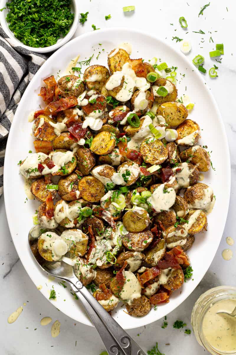Overhead shot of a large serving platter with roasted potato salad garnished with bacon and parsley