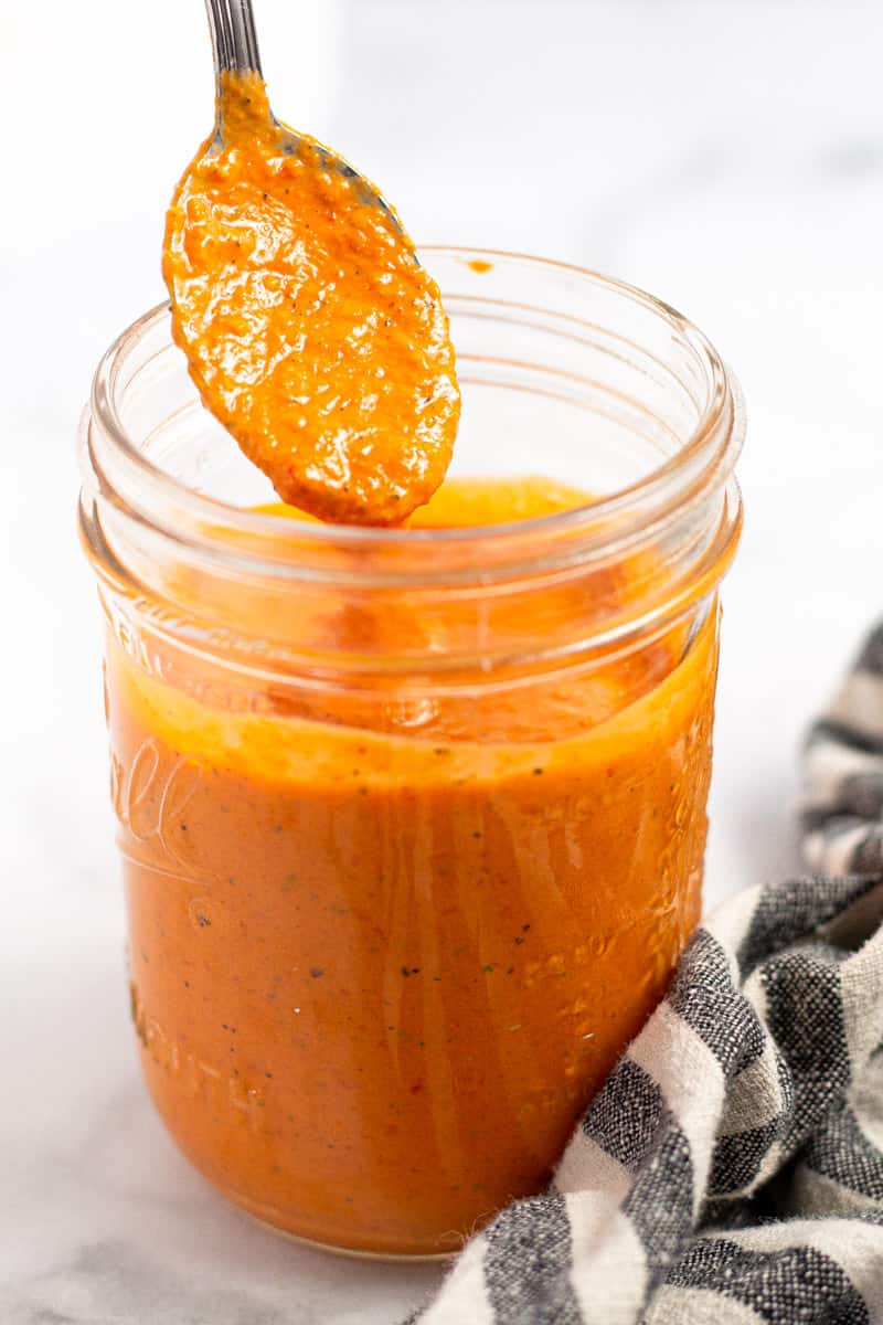 Spoon scooping sun-dried tomato dressing out of a mason jar