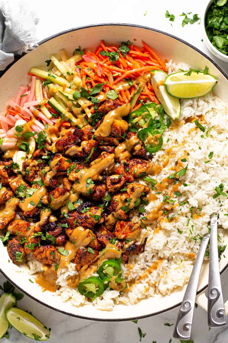 Overhead shot of a large white pan filled with Thai chicken and rice drizzled with peanut sauce