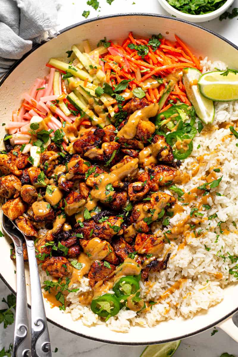 Overhead shot of a large white pan filled with Thai chicken and rice drizzled with peanut sauce