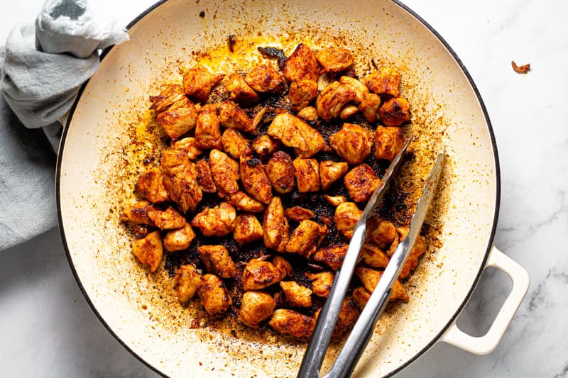Large white pan with sauteed diced chicken breast
