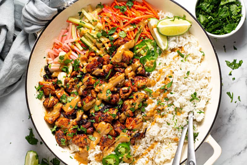 Overhead shot of a large white pan filled with Thai chicken and rice drizzled with peanut sauce