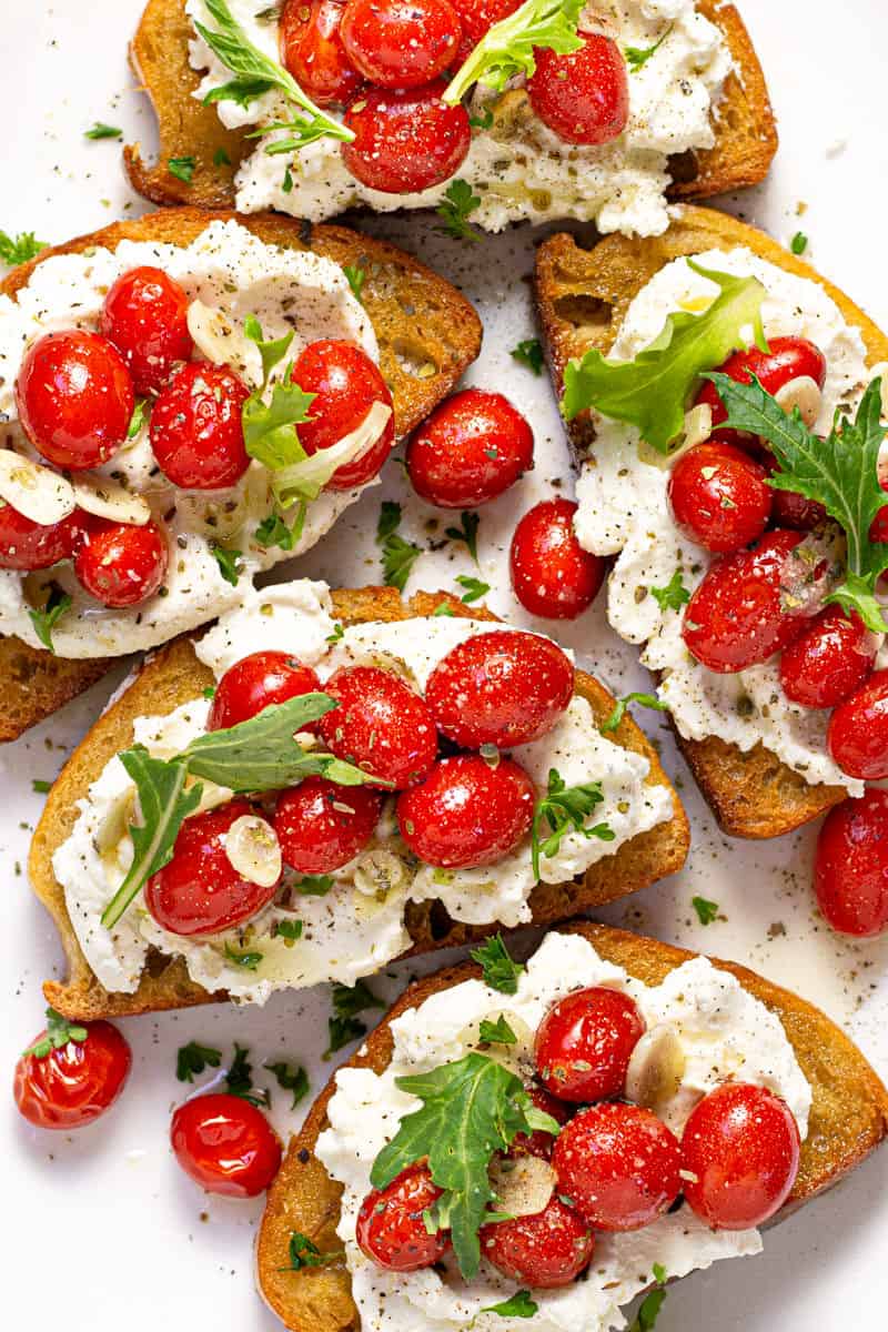 Overhead shot of roasted tomatoes on toast with ricotta and arugula