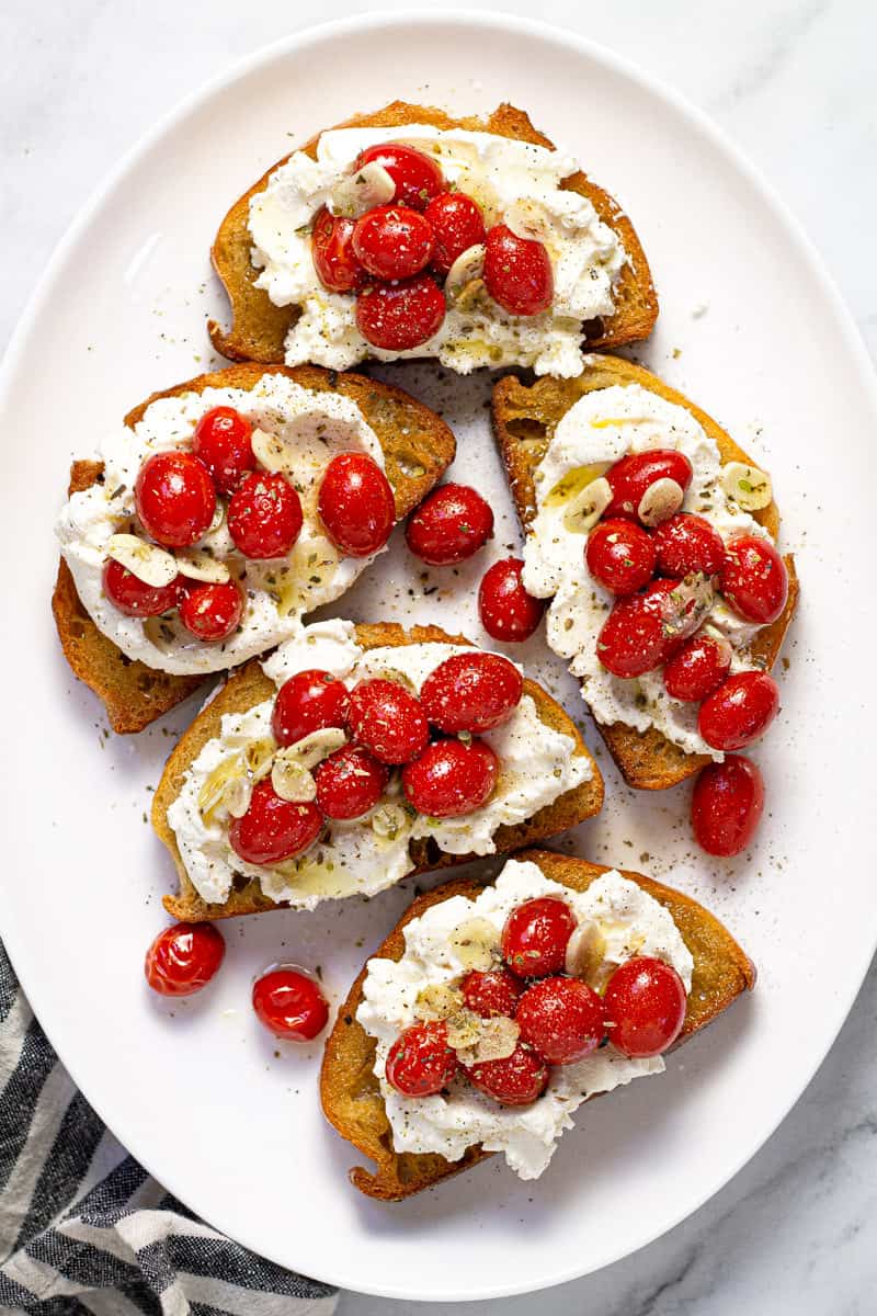 Large white platter with roasted tomatoes and garlic on top of toast with ricotta