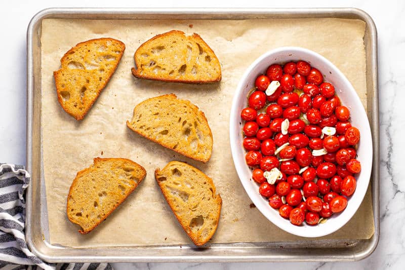Baking sheet with 5 slices of toast and a baking dish with roasted grape tomatoes