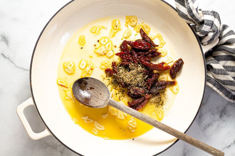 Large white pan with oil sliced garlic sun dried tomatoes and oregano