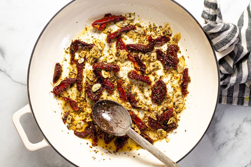 Large white pan with oil sliced garlic sun dried tomatoes and oregano