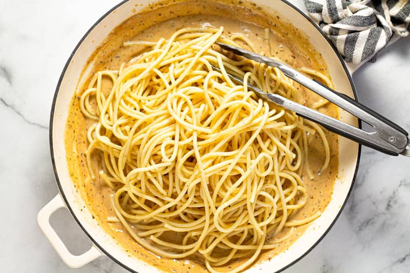 Overhead shot of a large white pan with al dente pasta and sun dried tomato cream sauce