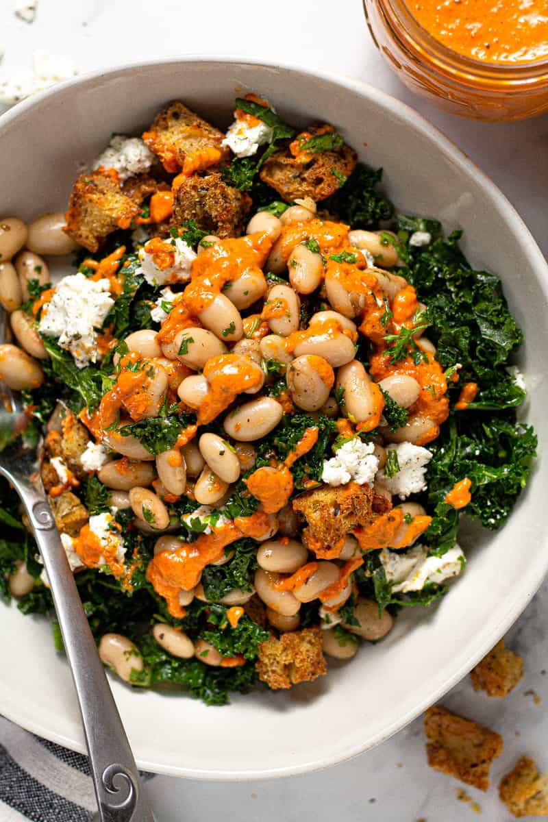 White bowl filled with massaged kale salad drizzled with sun-dried tomato dressing