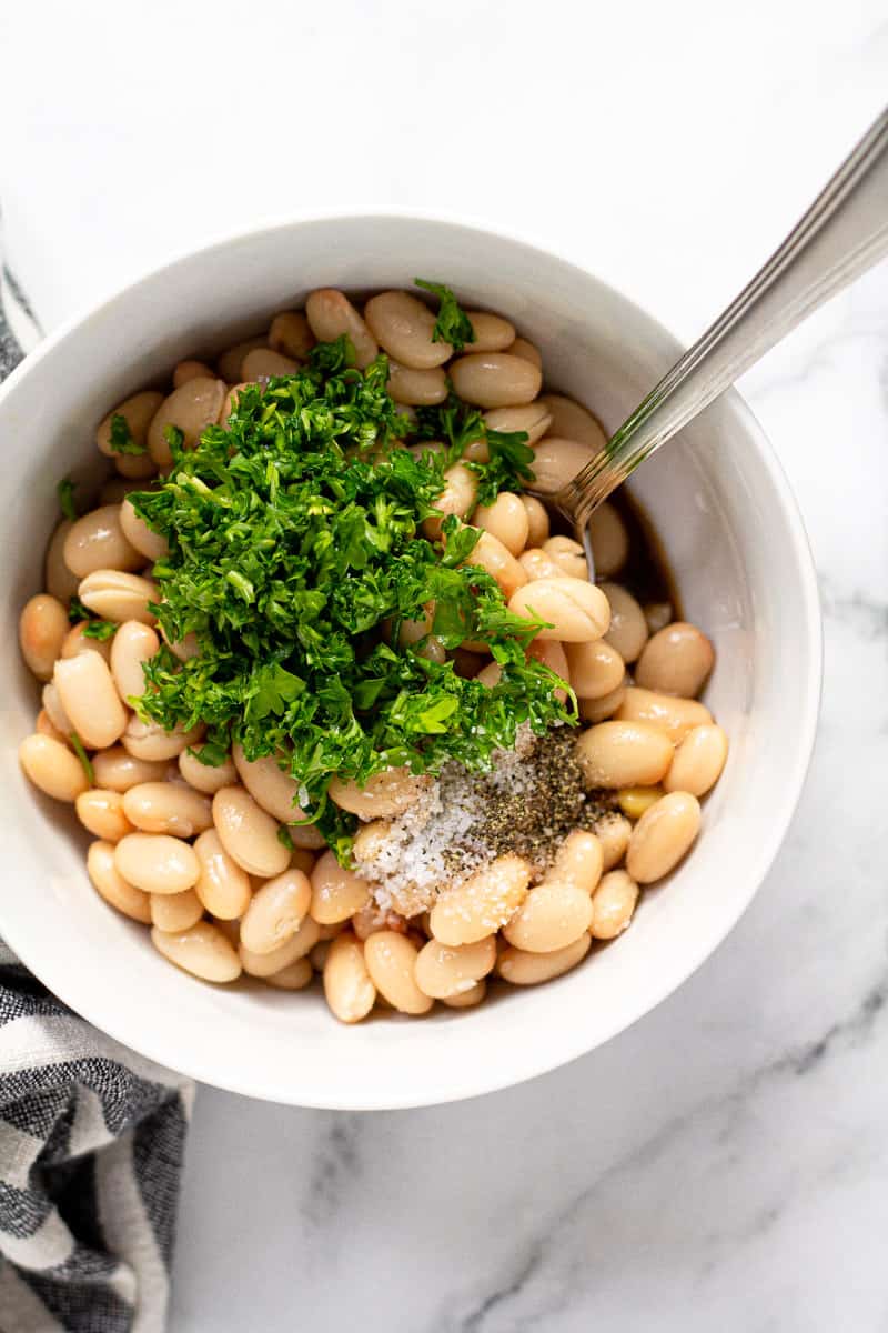 White bowl with Great Northern beans fresh parsley salt and pepper