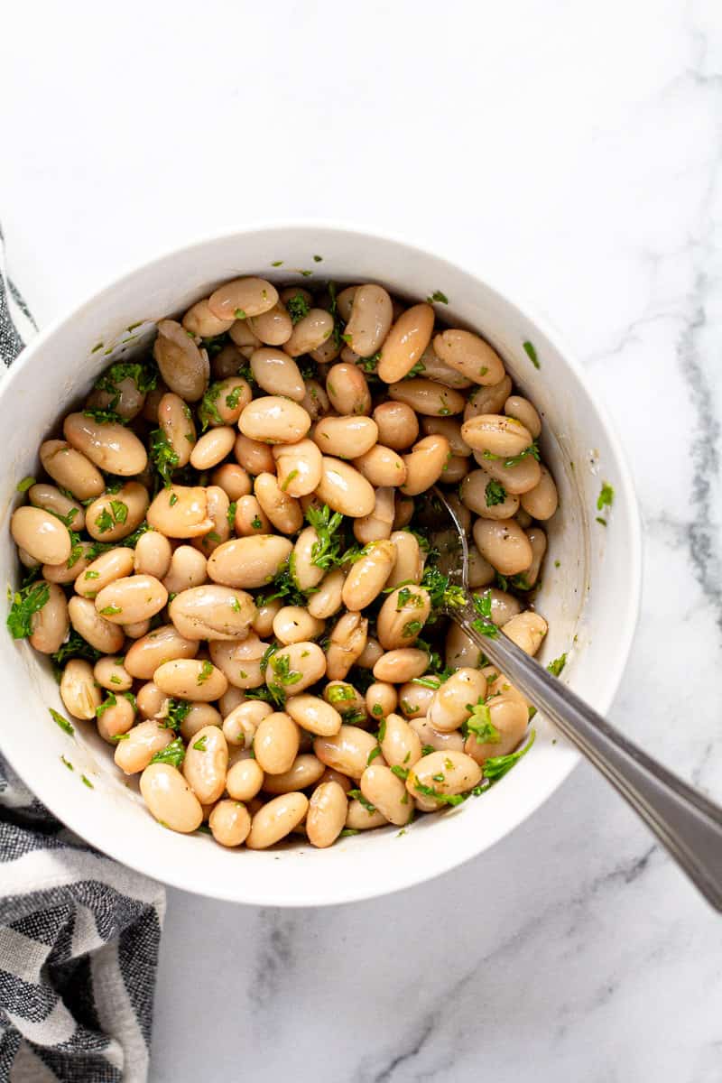 White bowl with Great Northern beans fresh parsley salt and pepper
