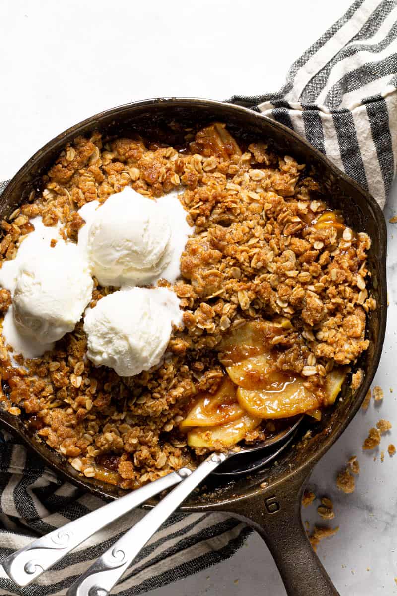 Large cast iron skillet filled with homemade apple crisp topped with vanilla ice cream 