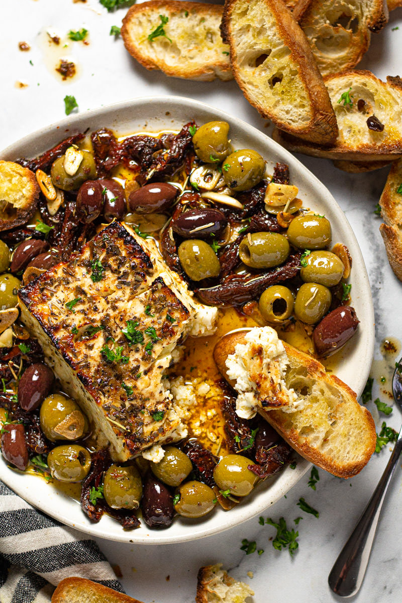 White plate filled with baked feta olives and herbs