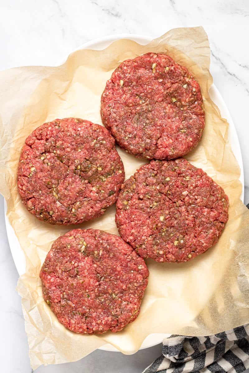 Four burger patties on a piece of parchment paper on a large platter