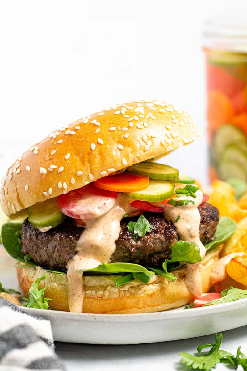 Close up shot of a Banh Mi burger topped with pickled veggies and drizzled with paprika mayo sauce