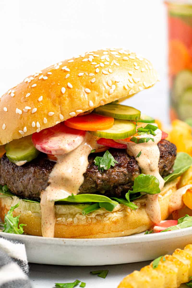 Close up shot of a Banh Mi burger topped with pickled veggies and drizzled with paprika mayo sauce