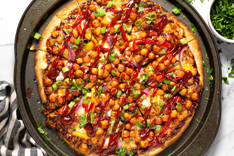 Round pizza pan with homemade chickpea veggie pizza garnished with cilantro 